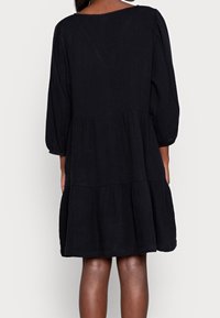 Svart, lager-på-lager klänning gjord av lätt tyg, med trekvartslånga ärmar och rundad hals, med en svepande silhuett.