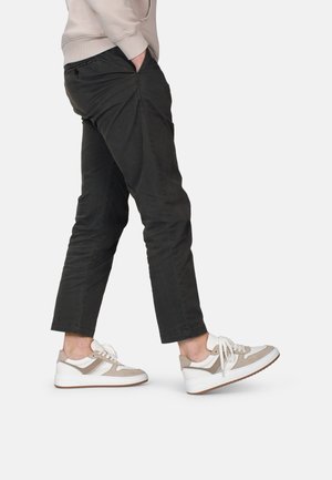 Zapatillas beige con acentos blancos y paneles texturizados, combinadas con pantalones ajustados negros. Los pantalones tienen bolsillos laterales y un diseño ajustado.