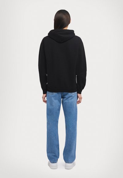 Schwarzer Kapuzenpullover mit lockerer Passform; kombiniert mit hellblauen geraden Jeans und weißen Sneakers. Einfaches Design, keine sichtbaren Muster.