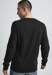 Black sweatshirt with long sleeves, crew neck, and ribbed cuffs. Smooth texture, minimal design, and a standard fit. Back view shown.