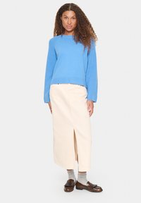 Pull en tricot bleu avec des poignets côtelés, associé à une jupe midi beige avec une fente à l'avant. Mocassins bruns portés par-dessus des chaussettes grises.