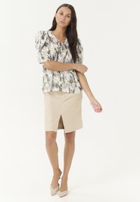 Lightweight, patterned blouse with puff sleeves, and a round neckline featuring a tie, paired with a knee-length beige skirt with a front slit.