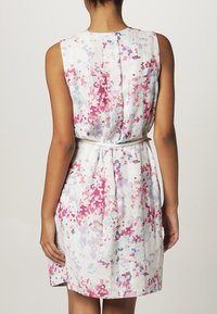 Rückansicht einer Person in einem ärmellosen, taillierten Kleid mit einem pinken, roten und blauen pixelierten Muster auf weißem Hintergrund.