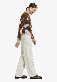 Maglione lavorato a maglia marrone e panna con motivo astratto, abbinato a pantaloni in velluto a coste color crema a gamba larga e stivaletti marrone scuro alla caviglia.