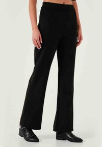 Schwarze, weite Hosen mit glatter Textur. Merkmale einen taillierten Bund und Reißverschlüsse am Knöchel, kombiniert mit schwarzen Stiefeletten.