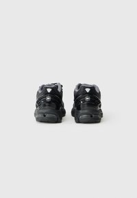 Chaussures de sport noires avec un dessus en maille texturée, un talon de soutien et une semelle rembourrée. Présentent des accents réfléchissants pour la visibilité.