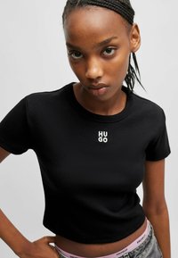 Black cotton crop t-shirt featuring a round neck and a small white "HUGO" logo on the chest. Smooth texture with short sleeves.