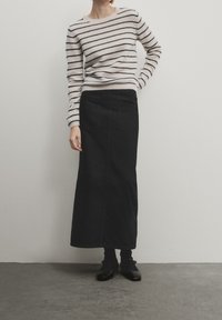 Pull léger rayé en crème et marine ; associé à une longue jupe en denim noire. La jupe possède des poches et une silhouette droite. Chaussures noires.