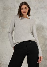 Lichtgrijze trui met een gestructureerd, ribbelpatroon, voorzien van een brede halslijn en lange mouwen, gecombineerd met zwarte broek.