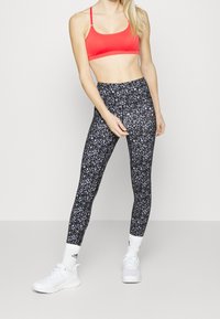 Legginsy w czarno-leopardzi wzór z wysokim stanem, zestawione z jasnoczerwoną sportową biustonoszem. Białe buty sportowe dopełniają strój.
