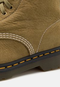 Stivale in pelle marrone con un upper testurizzato, cuciture bianche a contrasto e una suola in gomma nera e gialla con un motivo rigato.