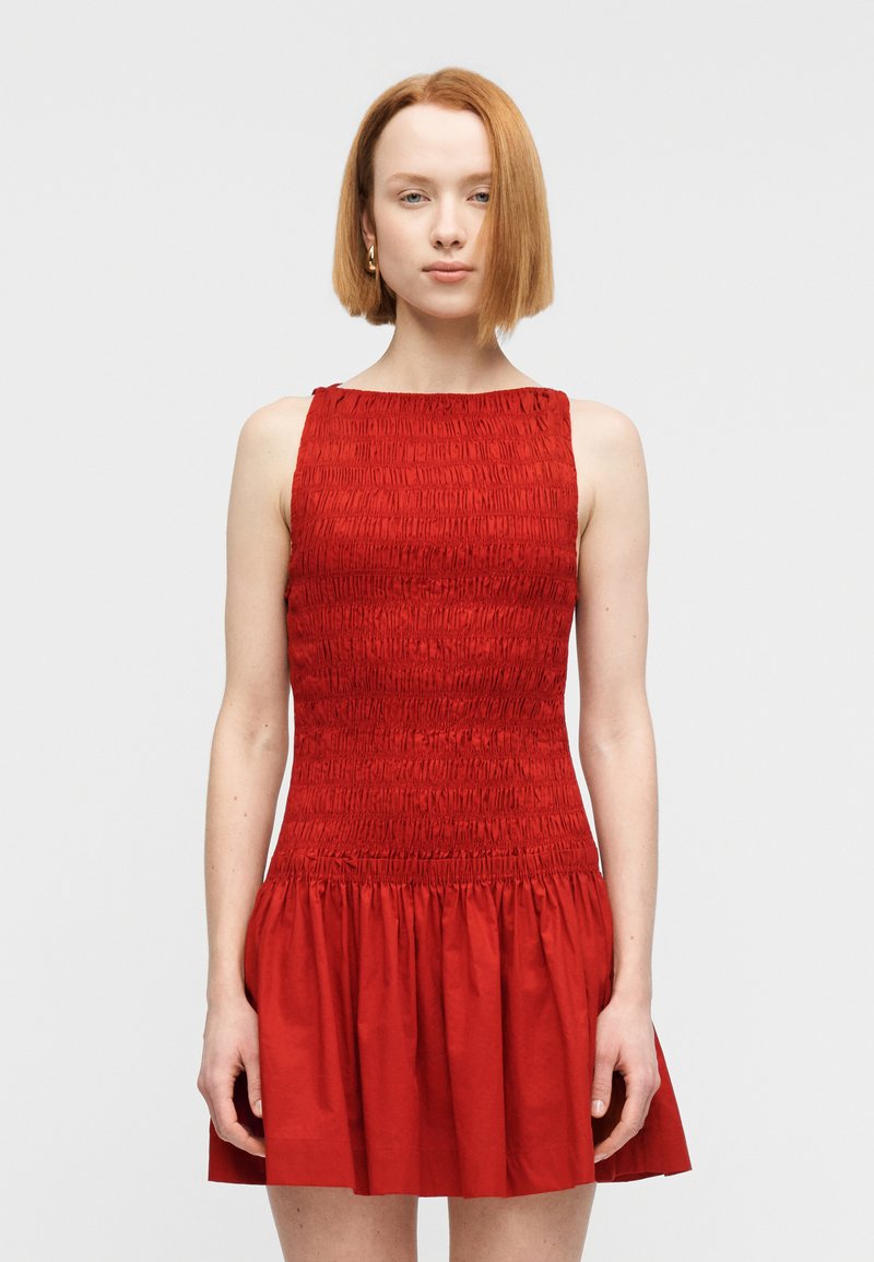 Κόκκινο αμάνικο φόρεμα με σφηκοφωλία στο μπούστο και φουσκωτή φούστα, υφή υφάσματος, στρογγυλή λαιμόκοψη και παιχνιδιάρικη σιλουέτα.