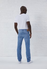 Faded blue denim jeans with a straight-leg cut, featuring back pockets and a brown label at the waistband, paired with a plain white t-shirt.