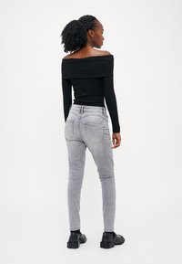 Vállnélküli, fekete bordás felső világosszürke, slim fit farmernadrággal párosítva. Jelentős részletek közé tartozik az elülső és hátsó zseb, valamint a testhez álló fazon.