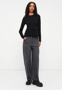 Top negro de manga larga con textura canalé combinado con pantalones de mezclilla gris de pierna ancha. Zapatos negros de suela gruesa completan el atuendo. Fondo liso.
