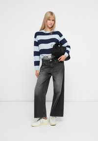 Striped sweater in light blue and navy, gray wide-leg jeans with a cut hem, and white sneakers. Holding a black pouch bag.