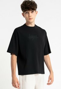 Czarna, oversize koszulka wykonana z bawełny, z okrągłym dekoltem i krótkimi rękawami, ozdobiona subtelnym graficznym logo z przodu.