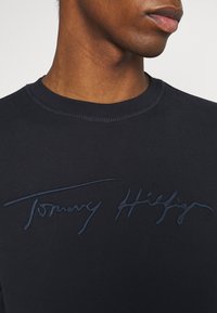 Navyblauwe katoenen sweatshirt met een ronde hals en een gedetailleerd donkerblauw geborduurd logo "Tommy Hilfiger" over de borst.