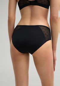 Black briefs with a smooth front, lace side panels featuring a geometric pattern, and soft elastic waistband, offering a snug fit.