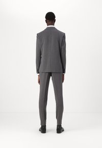 Costume gris sur mesure comprenant une veste à simple boutonnage et un pantalon slim, confectionné dans un tissu lisse avec une texture subtile.