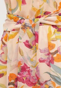 Tissu à motif floral dans des teintes pastel avec des nuances de rose, d'orange et de vert. Présente une ceinture nouée à la taille et une texture douce et fluide.