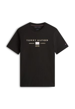 Maglietta nera a maniche corte con testo "Tommy Hilfiger American Classics EST. 1985" e logo sul petto, piccolo logo a bandiera sulla manica sinistra.