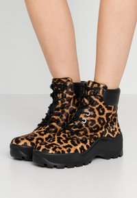 Ankle boty s leopardím potiskem vyrobené z měkkého umělého kožíšku, s černou gumovou podrážkou, černými koženými detaily a šněrováním se stříbrnými očky.