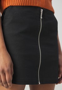 Melna džinsu svārki ar priekšējo sudraba rāvējslēdzēju un atklātu aparatūru. Iemēģinātas ir pielāgota dizaina un gludas tekstūras, nodrošinot mūsdienīgu izskatu.