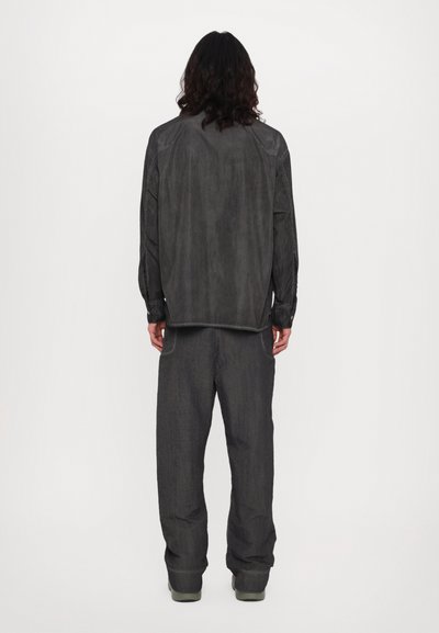 Ensemble ample de couleur gris foncé, comprenant un haut à manches longues et un pantalon à jambes larges avec une finition texturée et un design minimaliste.