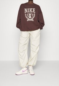 Vinröd Nike-tröja med vitt märke, krämfärgade baggybyxor och vita sneakers med lila detaljer. Enkel, avslappnad sportklädsel.