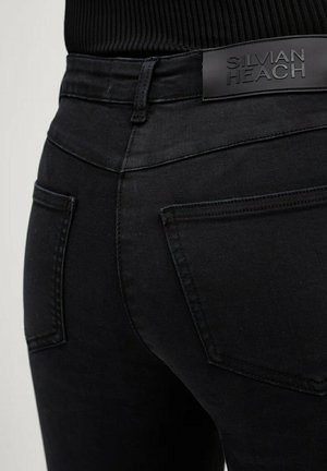 Primo piano della parte posteriore di jeans in denim nero con due tasche e un'etichetta del marchio nera "Silvian Heach" sulla vita.