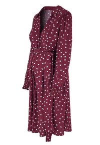 Burgundy klänning med vita prickar, knäppning framtill, långa ärmar med rynkade manchetter, justerbart midjeband och knälång fåll.