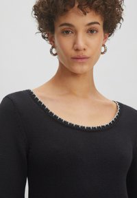 Schwarzer Pullover mit strukturiertem Strick, der einen runden Halsausschnitt mit einem kontrastierenden dekorativen Besatz aufweist.