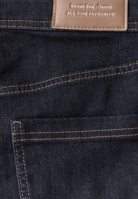 Tmavě modrá džínsovina se kontrastním světlým hnědým prošíváním, přední kapsou a koženou etiketou s nápisem "Street One - Denim".