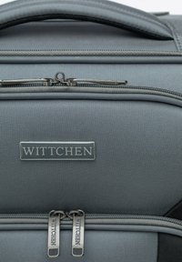 Grau farbige Reise Tasche aus Stoff mit strukturierter Oberfläche, ausgestattet mit einem oberen Griff und doppelten Reißverschluss-Schlüssen. Auf der Vorderseite ist ein silbernes "WITTCHEN"-Logo zu sehen.
