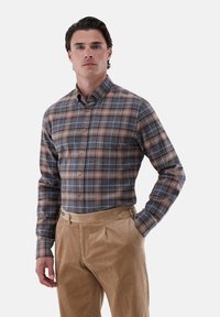 Braun-blau kariertes Hemd mit Knopfkragen, langen Ärmeln und glatter Textur, kombiniert mit hellbraunen Cordhosen.