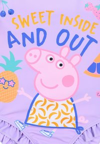 Lila Badebekleidung mit einem Cartoon-Schweinecharakter, der einen bananenbedruckten Oberteil trägt, umgeben von tropischen Designs und dem Text "SÜSSES INNEN UND AUßEN."