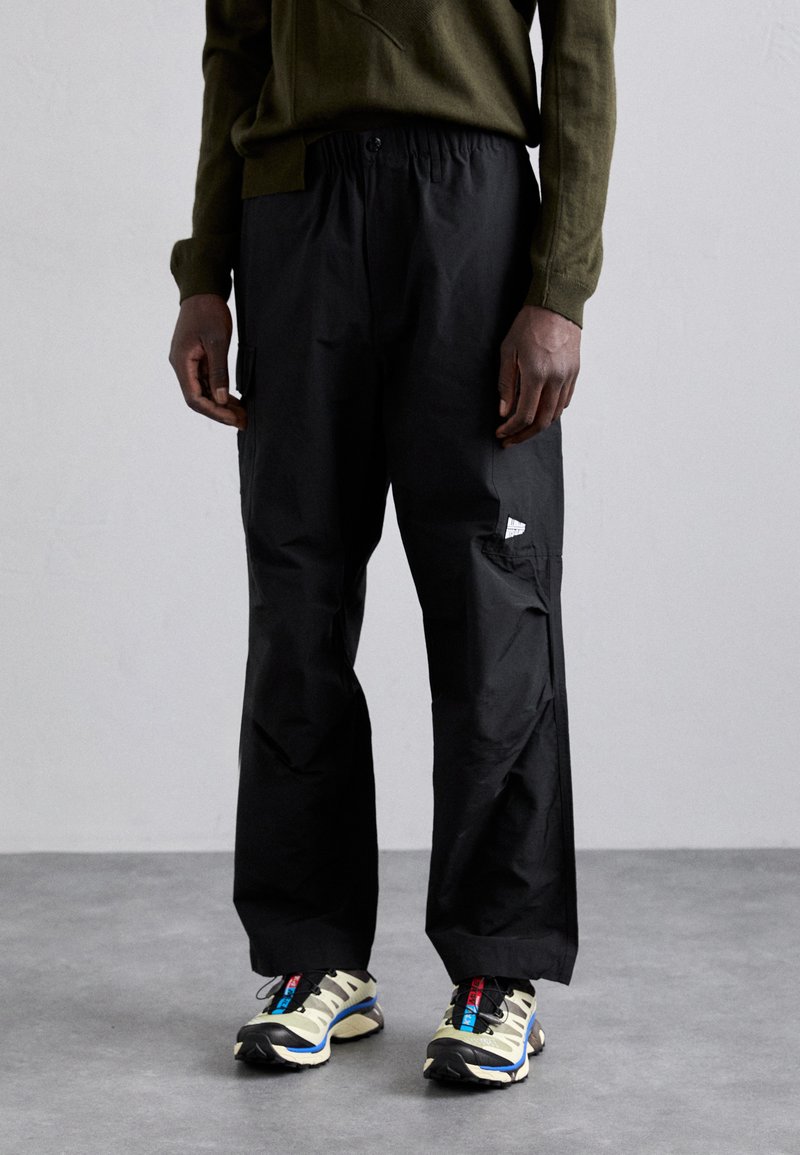 Svart cargo bukser med elastisk midje, med en sidelomme og et lite logomerke. Kombinert med flerfargede joggesko.