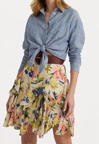 Sininen ja valkoinen raidallinen paitapusero, joka on solmittu vyötärölle, yhdistettynä kermaiseen kukkakuosisia hameeseen, jossa on kerroksellisia röyhelöitä ja ruskea vyö.