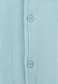 Tejido acanalado de color azul claro con dos botones azules a juego alineados verticalmente en una camisa o cárdigan.