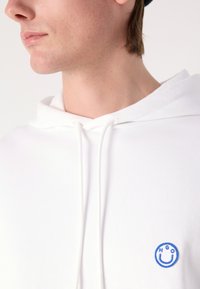 Hoodie bianco in cotone con cappuccio e logo ricamato blu circolare sul petto. Texture liscia e vestibilità comoda.