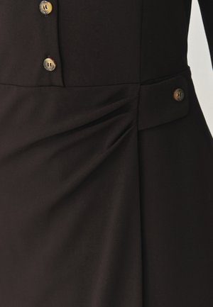 Zwart jurkstof met subtiele textuur, zijplooien en twee lichtbruine knopen op de taille voor detail en sluiting.