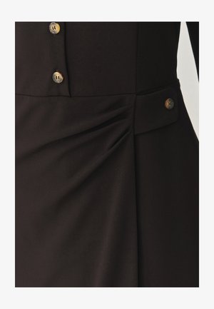 Čierna látka s jemnou textúrou, bočnými záhybmi a dvoma svetlohnedými gombíkmi v oblasti pásu pre ozdobu a zapínanie.