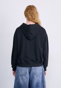Svart hettegenser med avslappet passform og ribbestrikket kant, parret med lyseblå vide jeans, som viser en uformell og komfortabel stil.