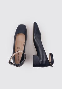 Pehar de cuero azul marino con punta cuadrada y tacón bajo. Presenta una correa en el tobillo con hebilla. Textura suave y diseño minimalista.