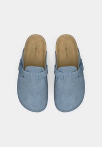 Μπλε σουέτ τσόκαρα με απαλό υφή, ανοιχτή πίσω πλευρά και ρυθμιζόμενο λουράκι. Φυσική ταμπά εσωτερική σόλα ορατή, μινιμαλιστικός σχεδιασμός, άποψη από πάνω.