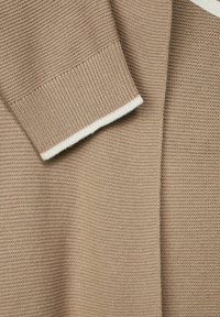 Beige stickad tröja med en strukturerad tyg, ribbad manschett och en kontrasterande vit rand i kanten.