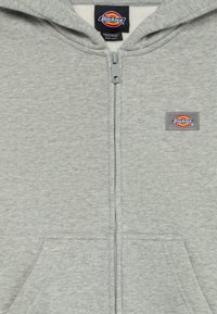 Pilkas užtrauktuku užsegamas džemperis, pagamintas iš minkštos medžiagos, su priekine kišene ir mažyčiu Dickies logotipu kairėje pusėje. Klasikinis dizainas.