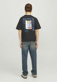 Camiseta negra de manga corta con un estampado gráfico colorido en la espalda, combinada con jeans azules holgados y una gorra marrón texturizada.