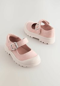 Zapatos Mary Jane de ante rosa con suela de goma blanca, punta redonda y correa ajustable con hebilla plateada. Detalles de superficie texturizada visibles.